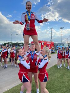 Tre cheerleaders i röda dräkter håller upp en topp.